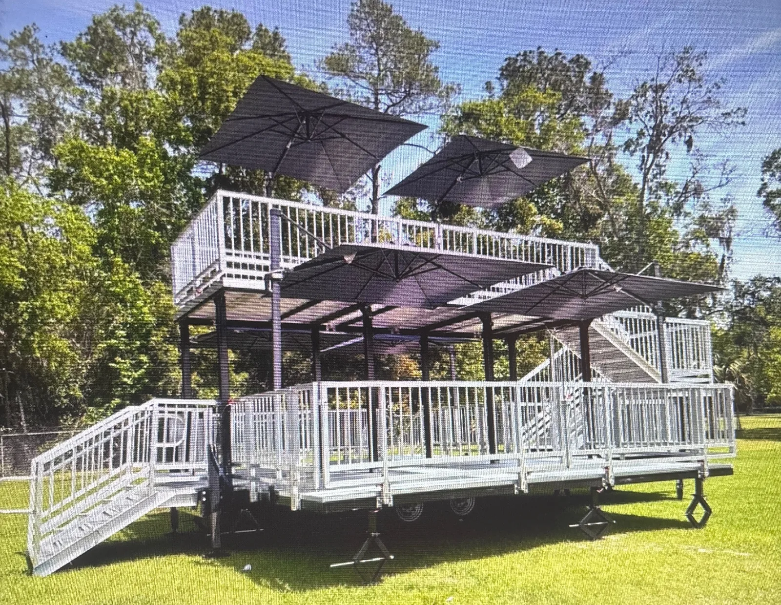 The Nest VIP deployed on grass — two-level deck with shade umbrellas, guardrails and side stairs